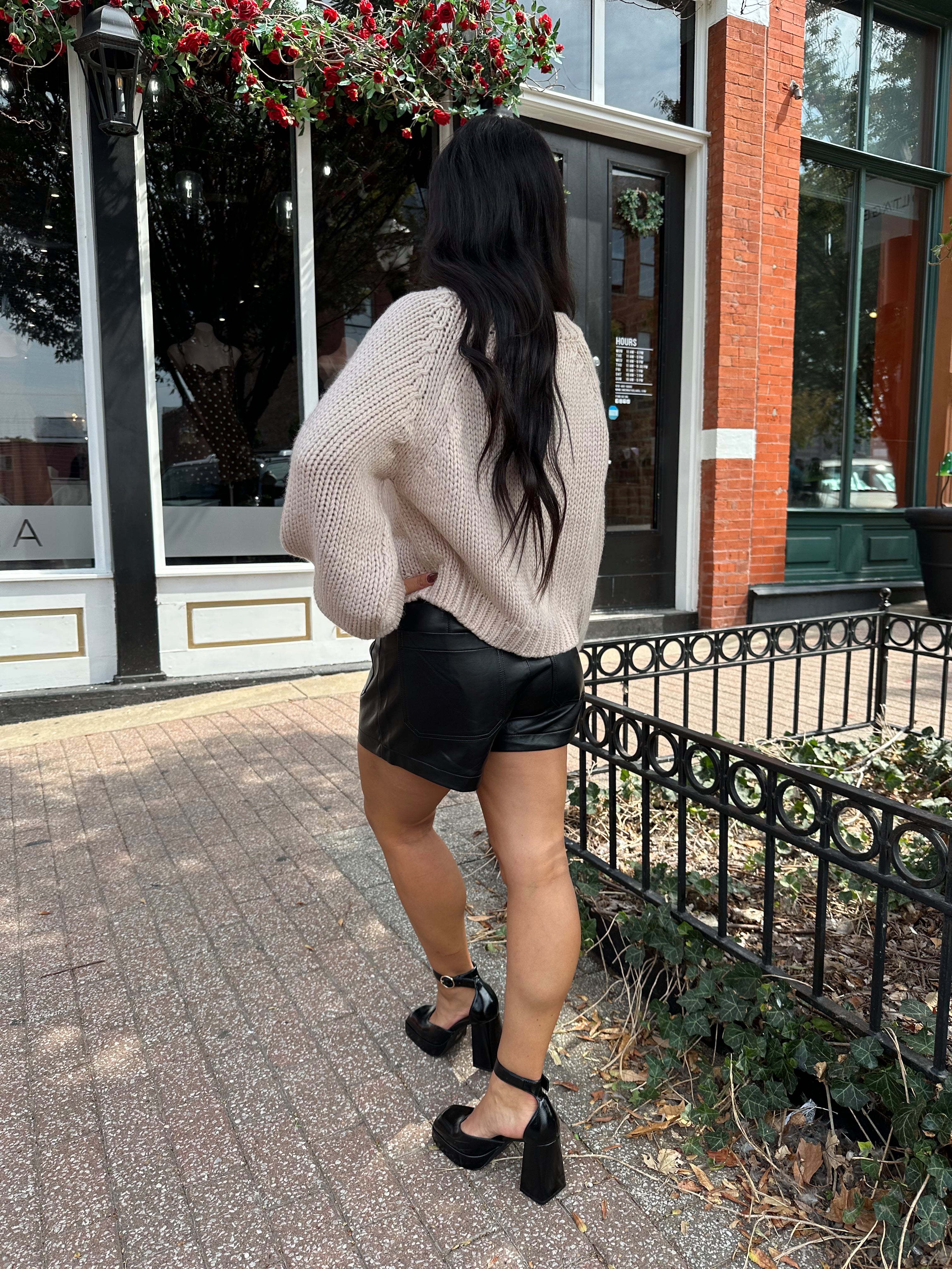 Woman wearing blush colored knit button down cardigan with black leather shorts.