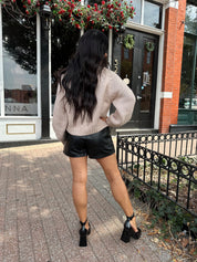 Woman wearing blush colored knit button down cardigan with black leather shorts.