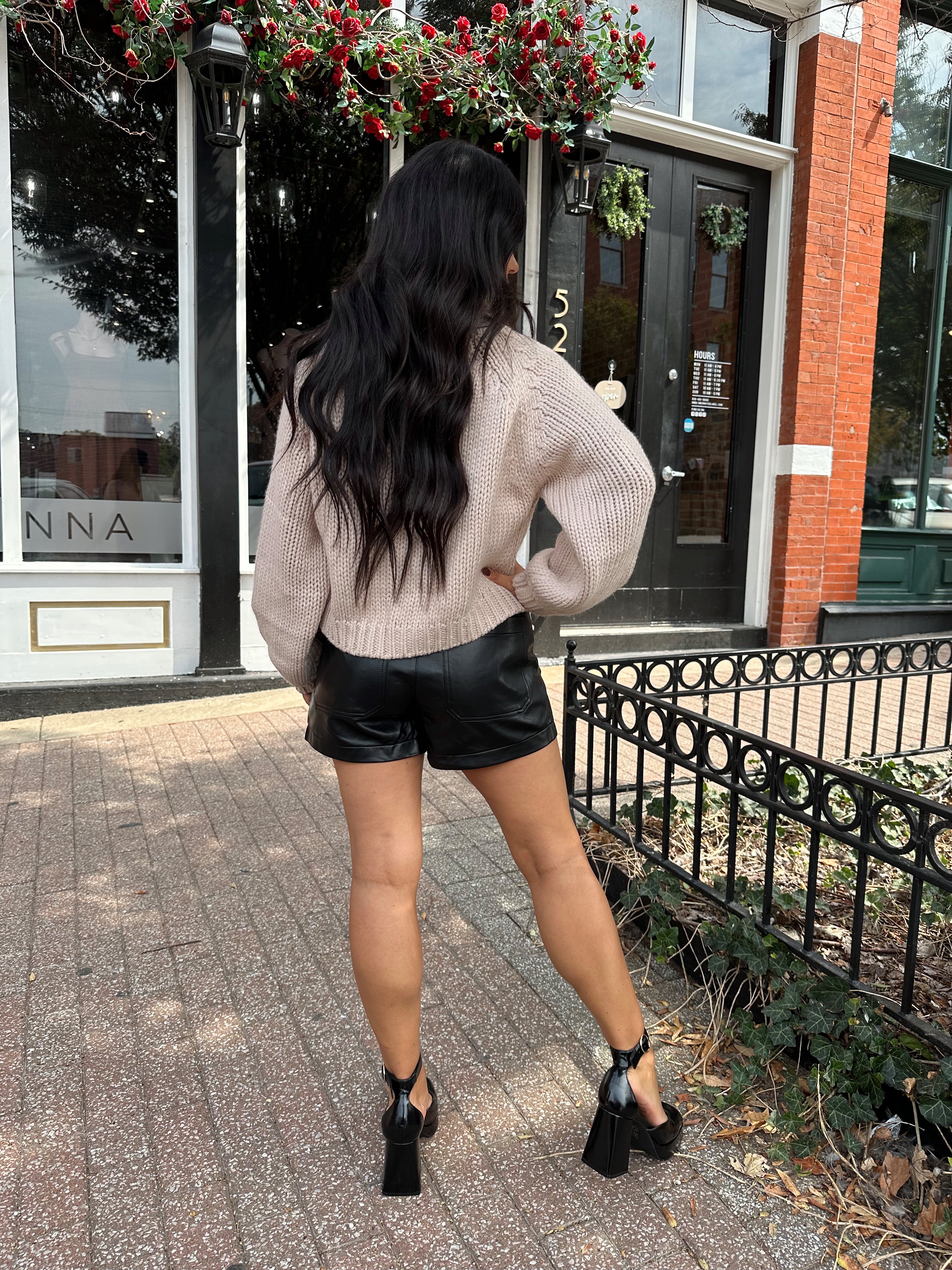 Woman wearing blush colored knit button down cardigan with black leather shorts.