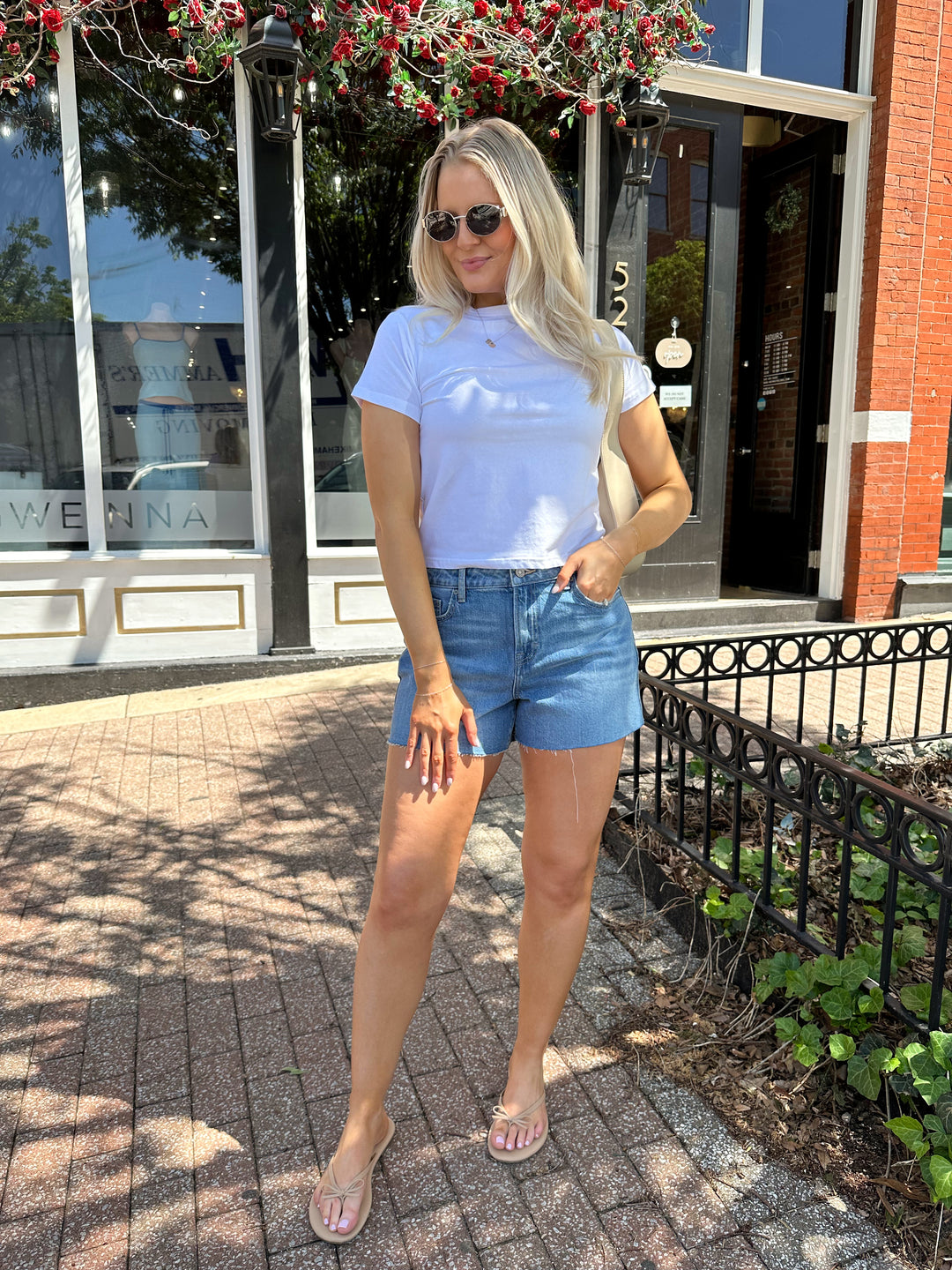 Woman wearing medium wash denim shorts with raw hem, and white t-shirt. 