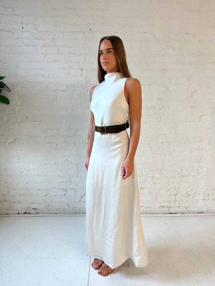 Woman wearing champagne colored satin maxi dress with high neck, and belted waist. 