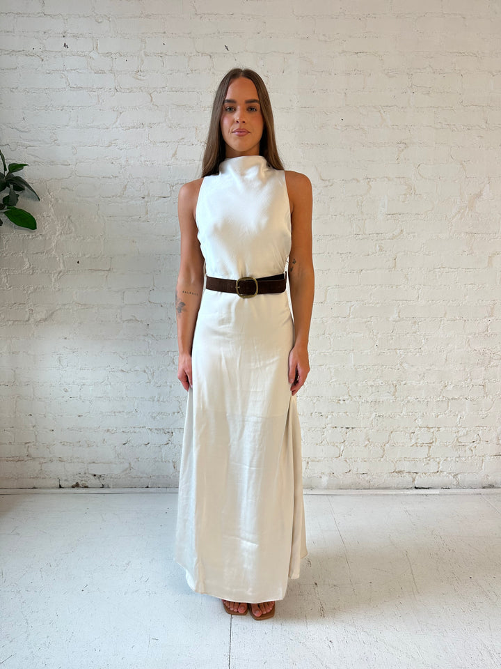 Woman wearing champagne colored satin maxi dress with high neck, and belted waist. 