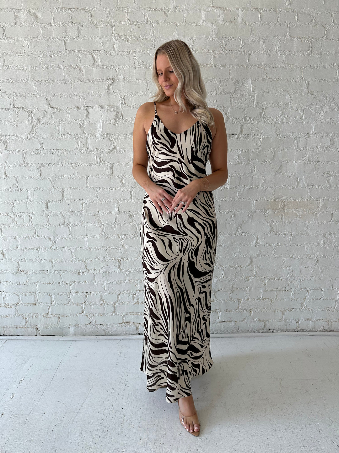 Woman wearing brown and cream abstract satin maxi dress with button detailing along the back.