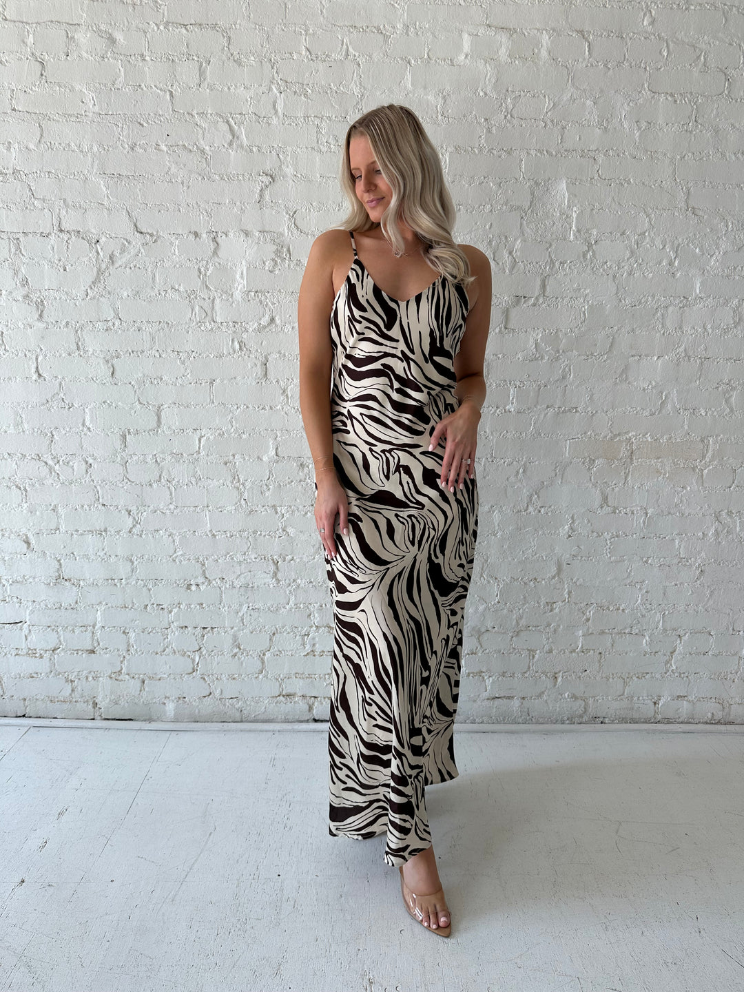 Woman wearing brown and cream abstract satin maxi dress with button detailing along the back.