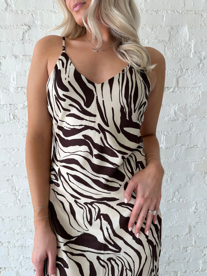 Woman wearing brown and cream abstract satin maxi dress with button detailing along the back.