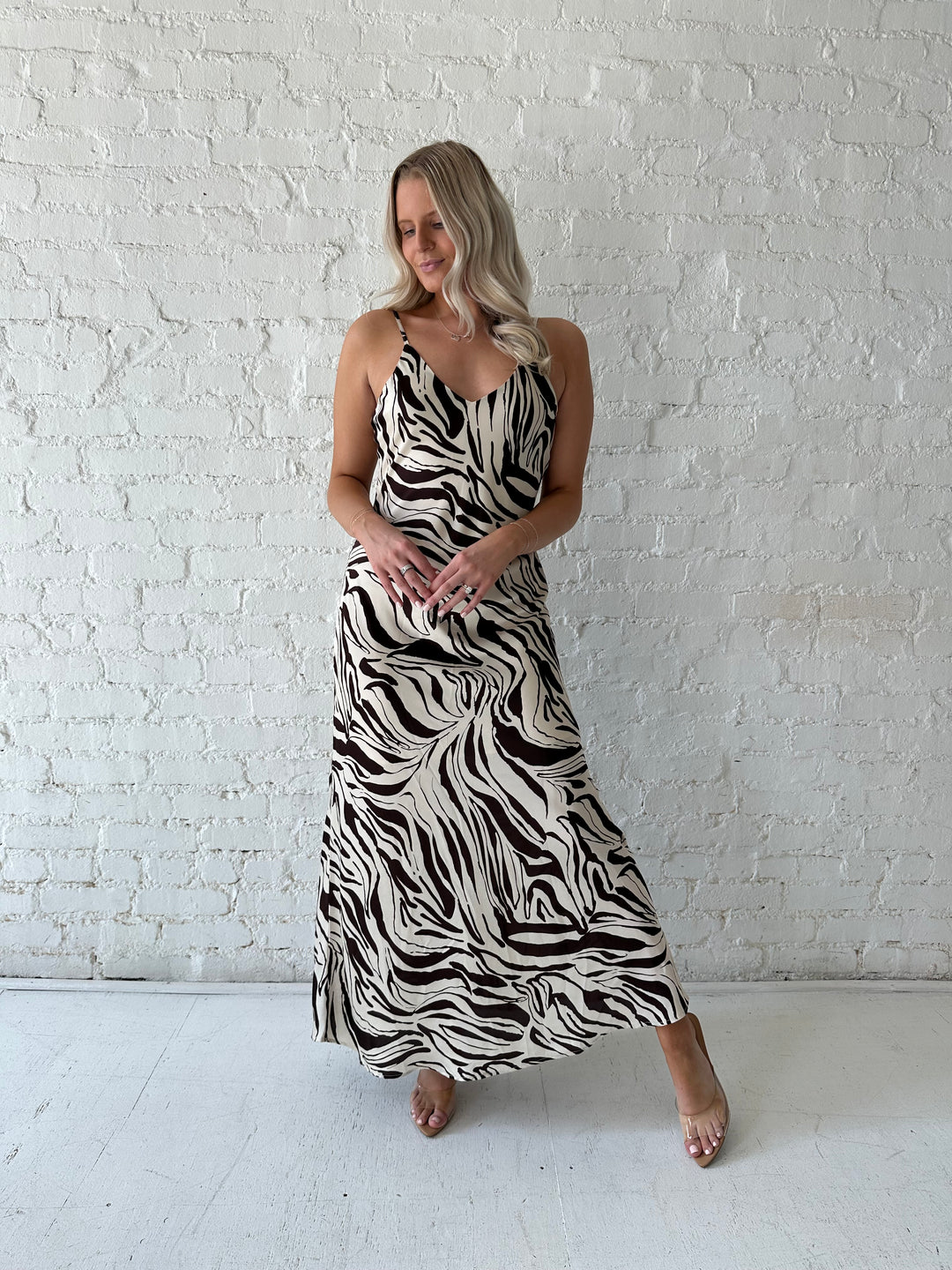 Woman wearing brown and cream abstract satin maxi dress with button detailing along the back.