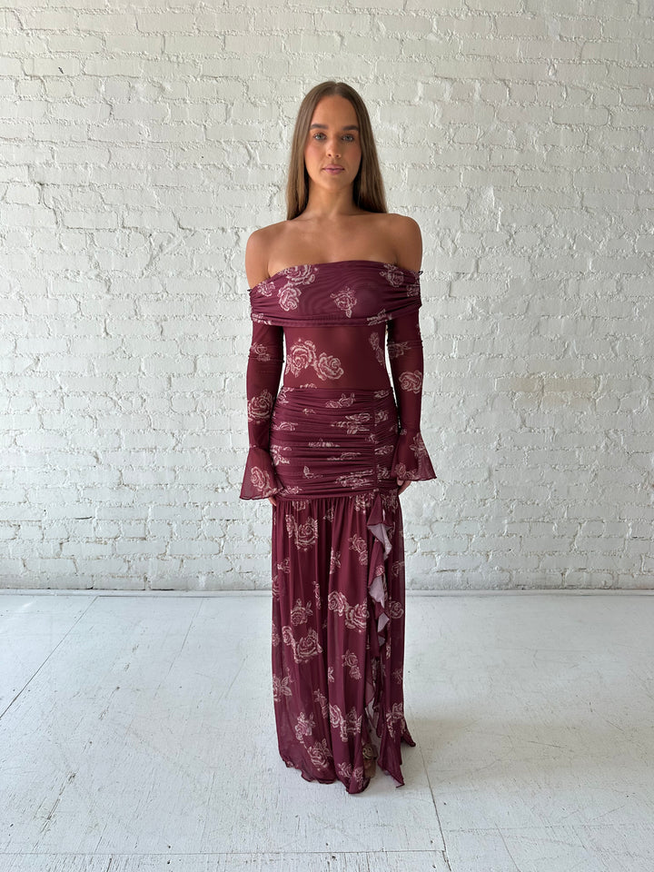 Woman wearing a purple floral mesh maxi dress with an off the shoulder neckline, and detachable scarf. 
