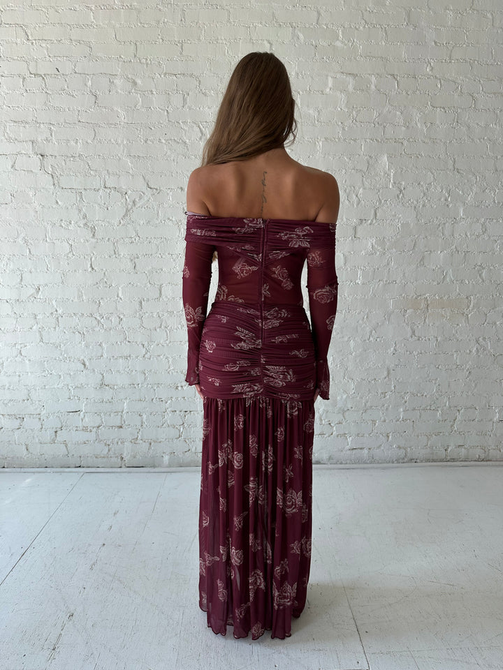 Woman wearing a purple floral mesh maxi dress with an off the shoulder neckline, and detachable scarf. 