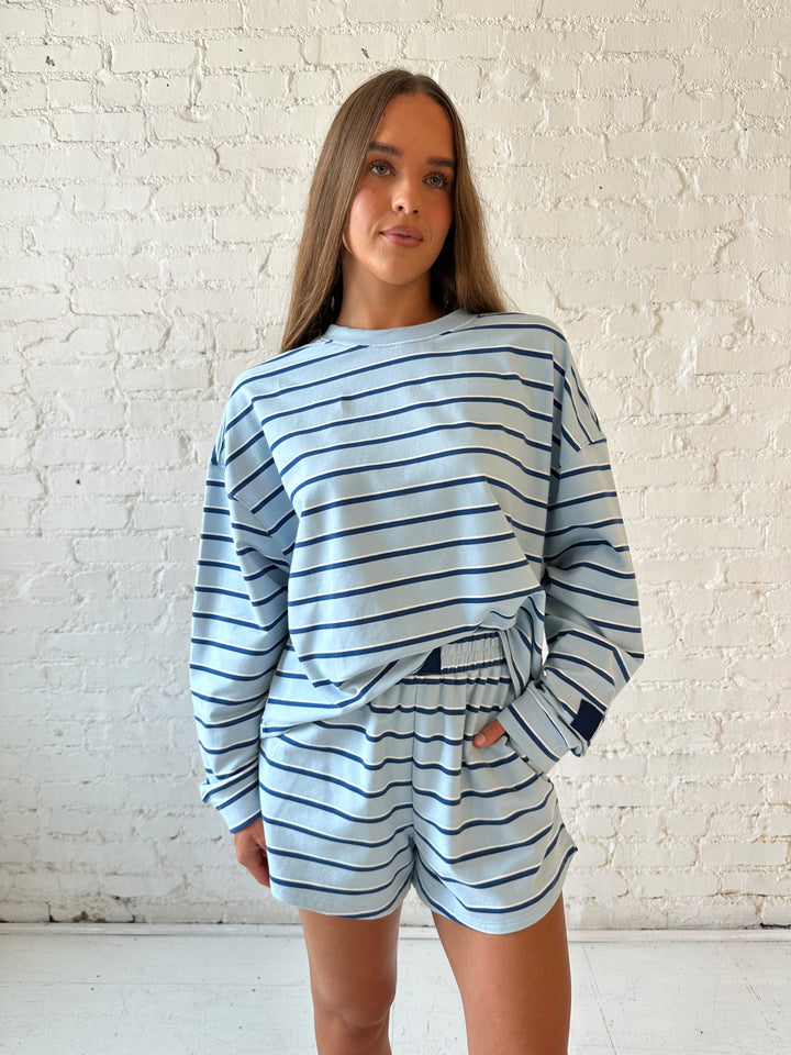 Woman wearing blue striped two piece long sleeve lounge set with flip flops.