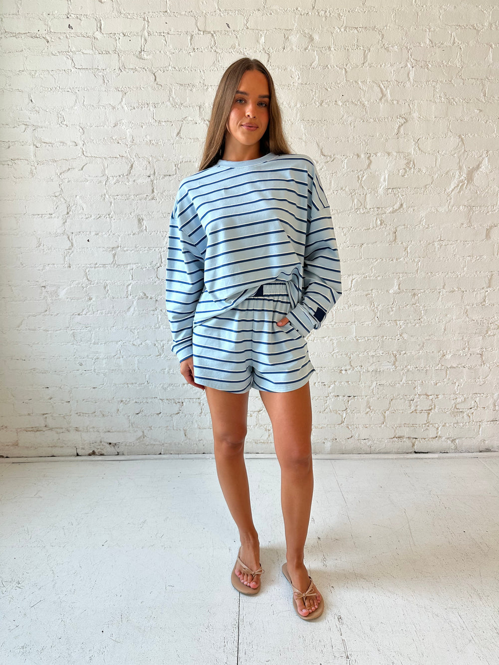 Woman wearing blue striped two piece long sleeve lounge set with flip flops.