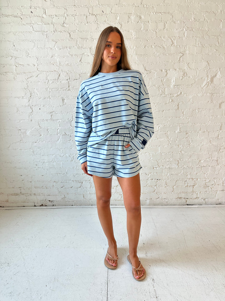 Woman wearing blue striped two piece long sleeve lounge set with flip flops.