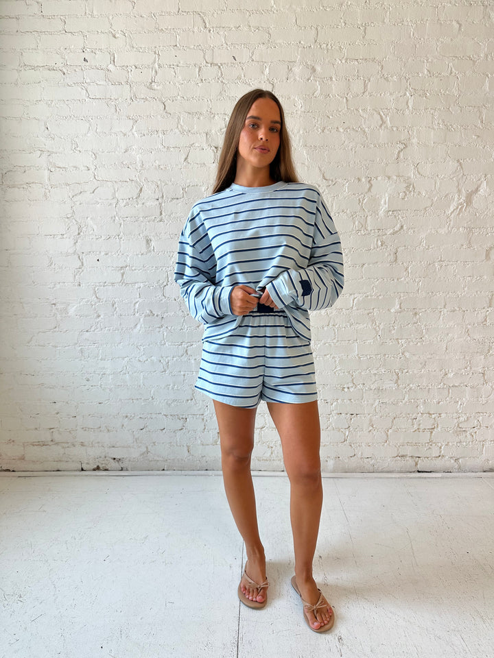 Woman wearing blue striped two piece long sleeve lounge set with flip flops.