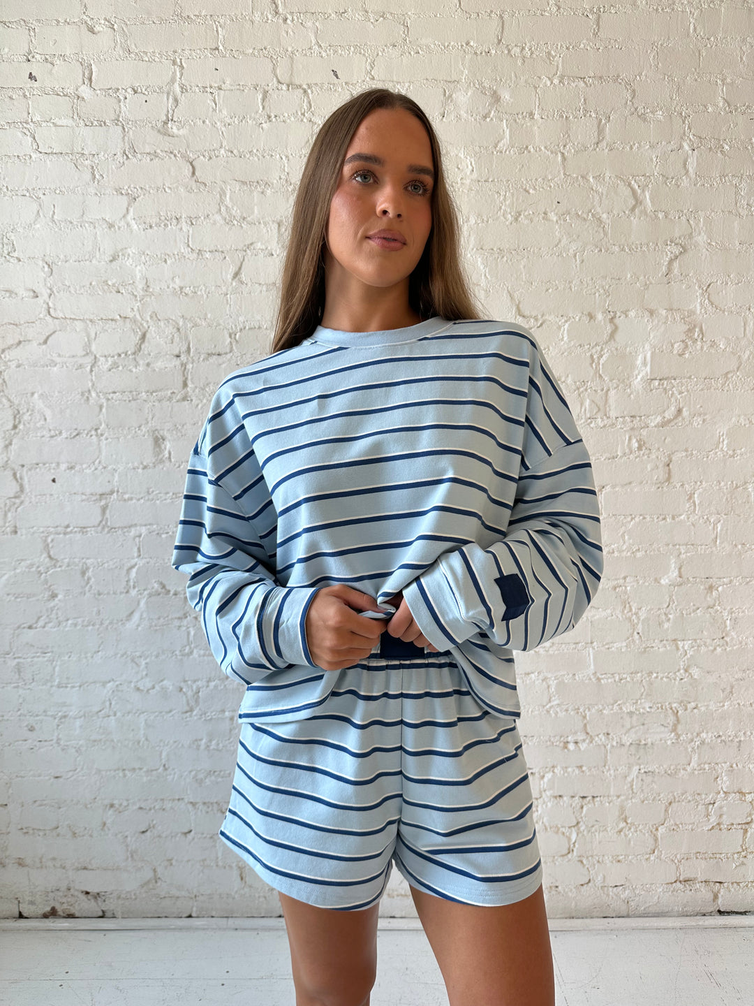 Woman wearing blue striped two piece long sleeve lounge set with flip flops.
