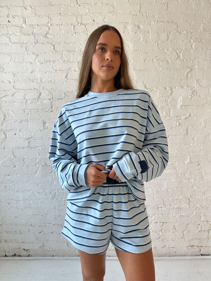 Woman wearing blue striped two piece long sleeve lounge set with flip flops.