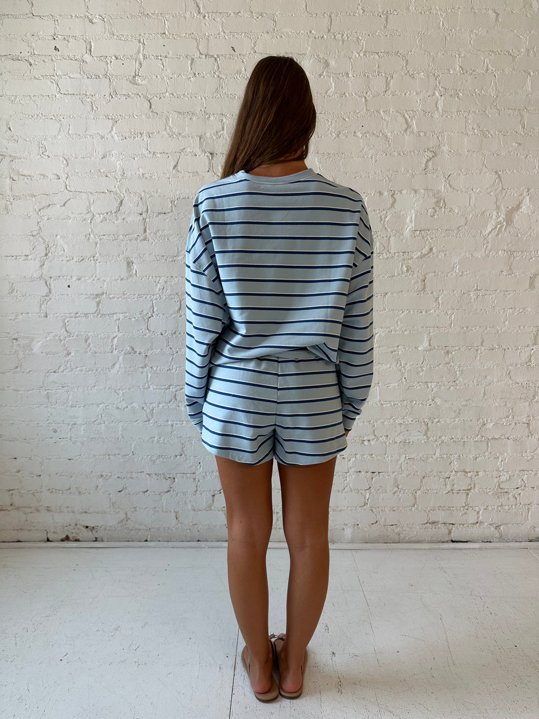Woman wearing blue striped two piece long sleeve lounge set with flip flops.