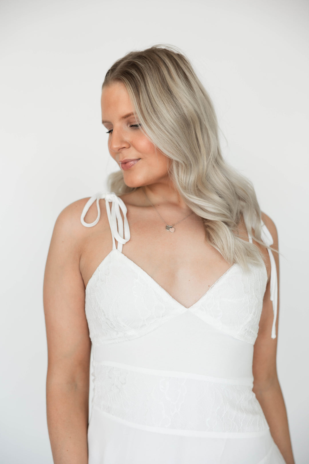Woman wearing white mini dress with delicate lace detailing and tie straps.
