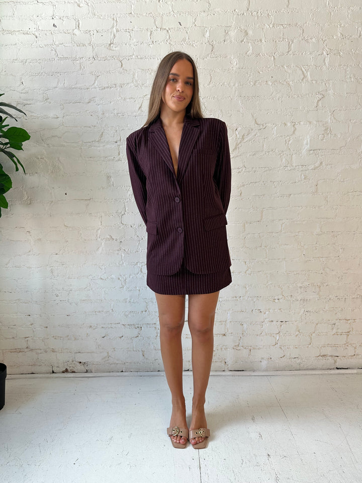 Woman wearing burgundy striped two piece skirt set with oversized blazer top.