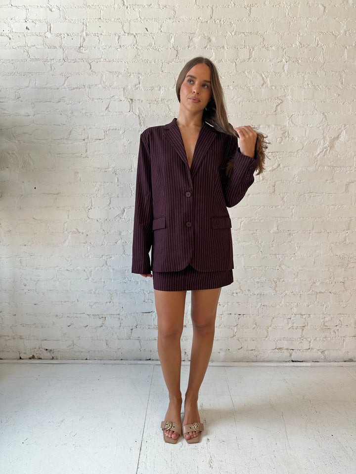 Woman wearing burgundy striped two piece skirt set with oversized blazer top.