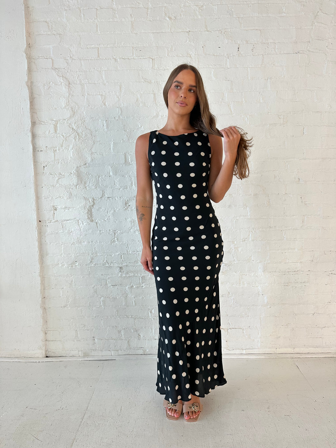 Woman wearing black and white polka dot high neck maxi dress with tan heels.