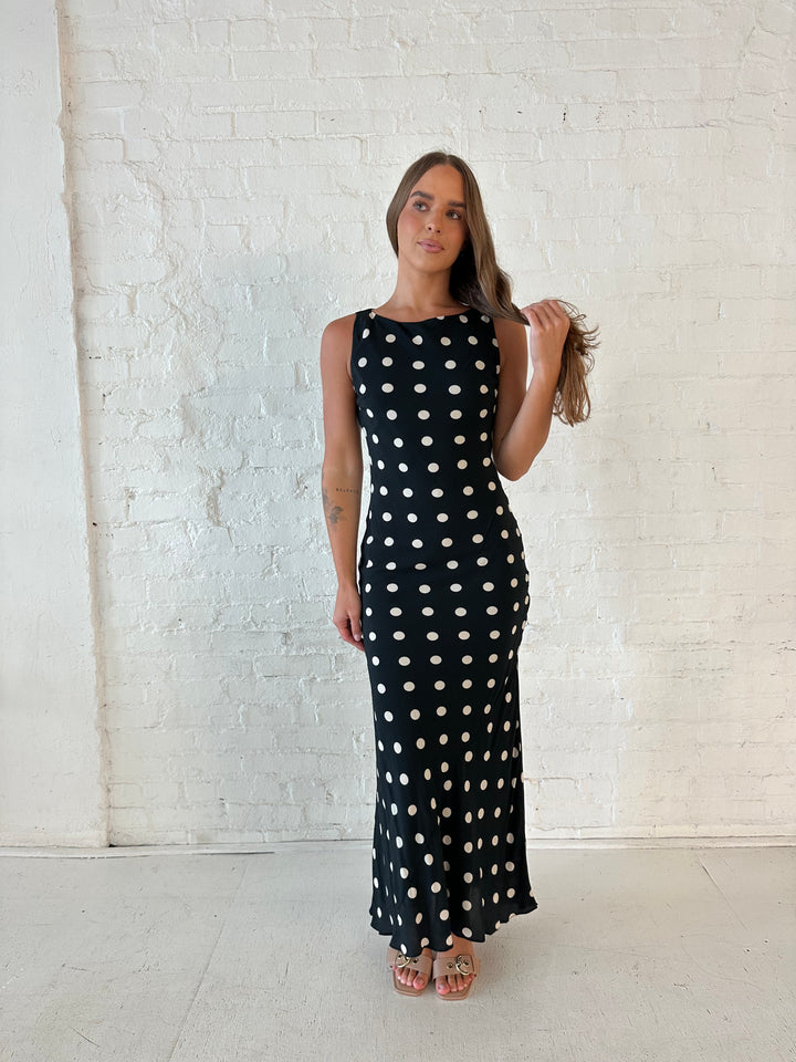 Woman wearing black and white polka dot high neck maxi dress with tan heels.