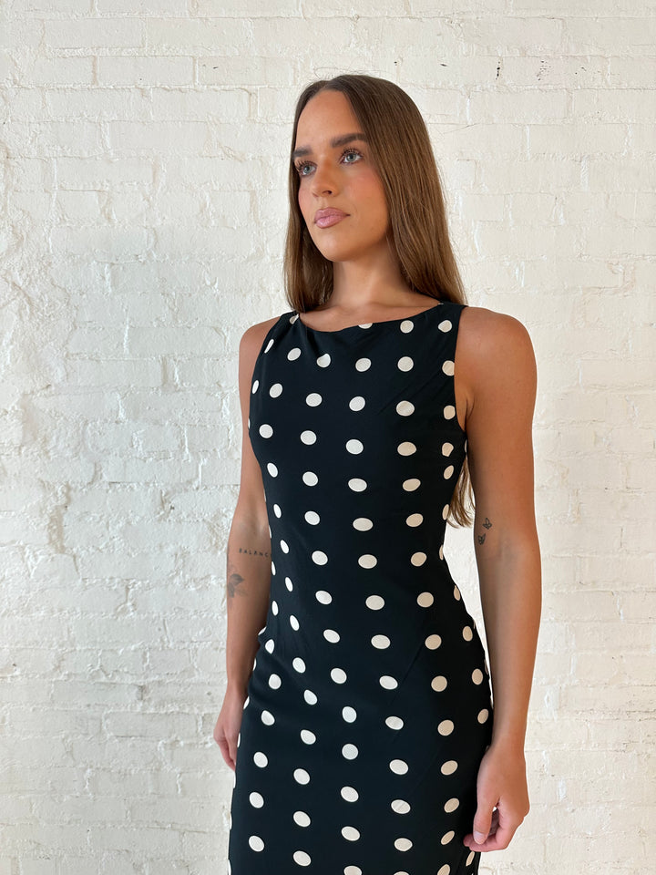 Woman wearing black and white polka dot high neck maxi dress with tan heels.