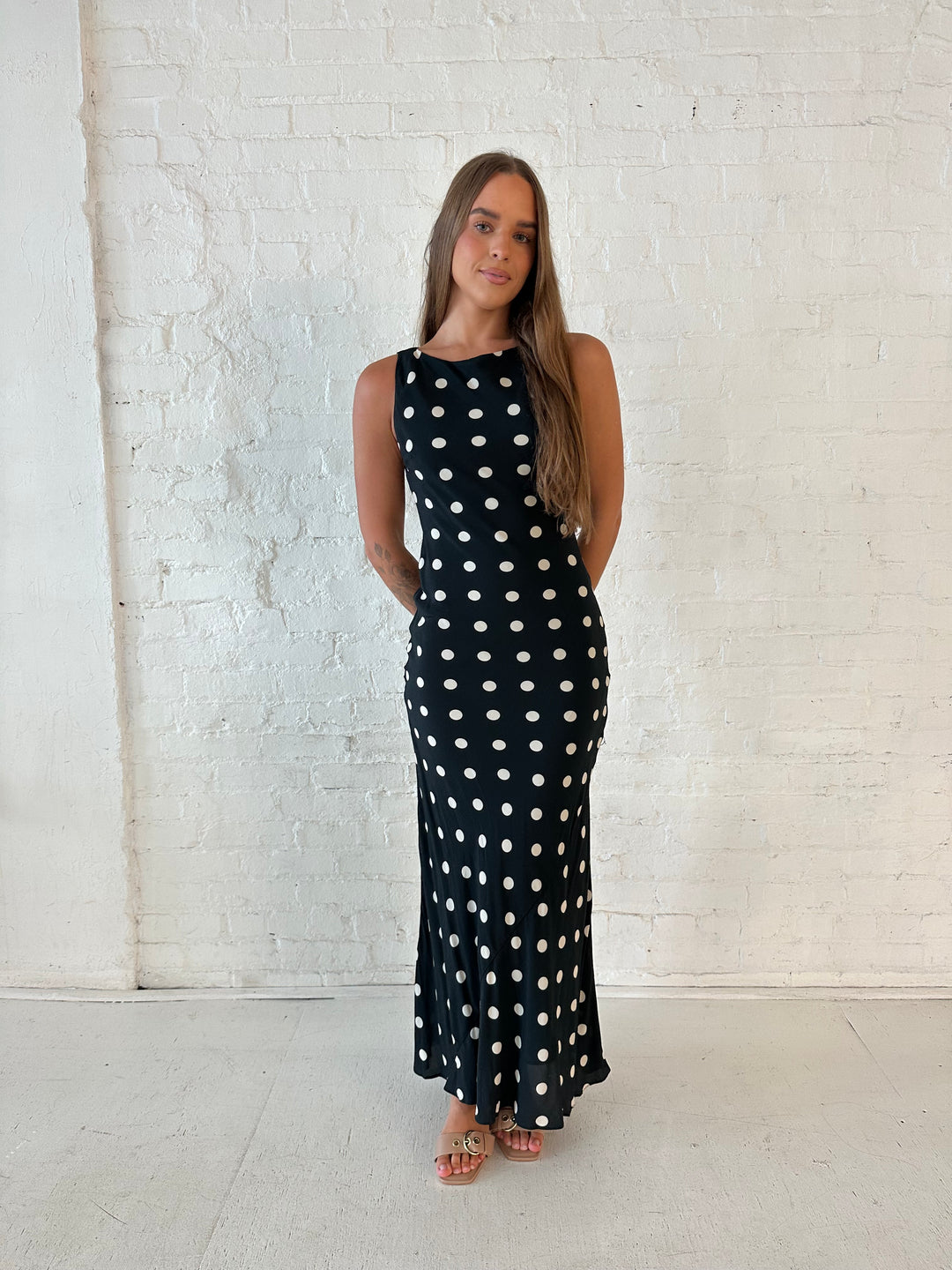 Woman wearing black and white polka dot high neck maxi dress with tan heels.