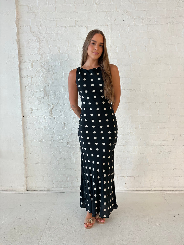 Woman wearing black and white polka dot high neck maxi dress with tan heels.