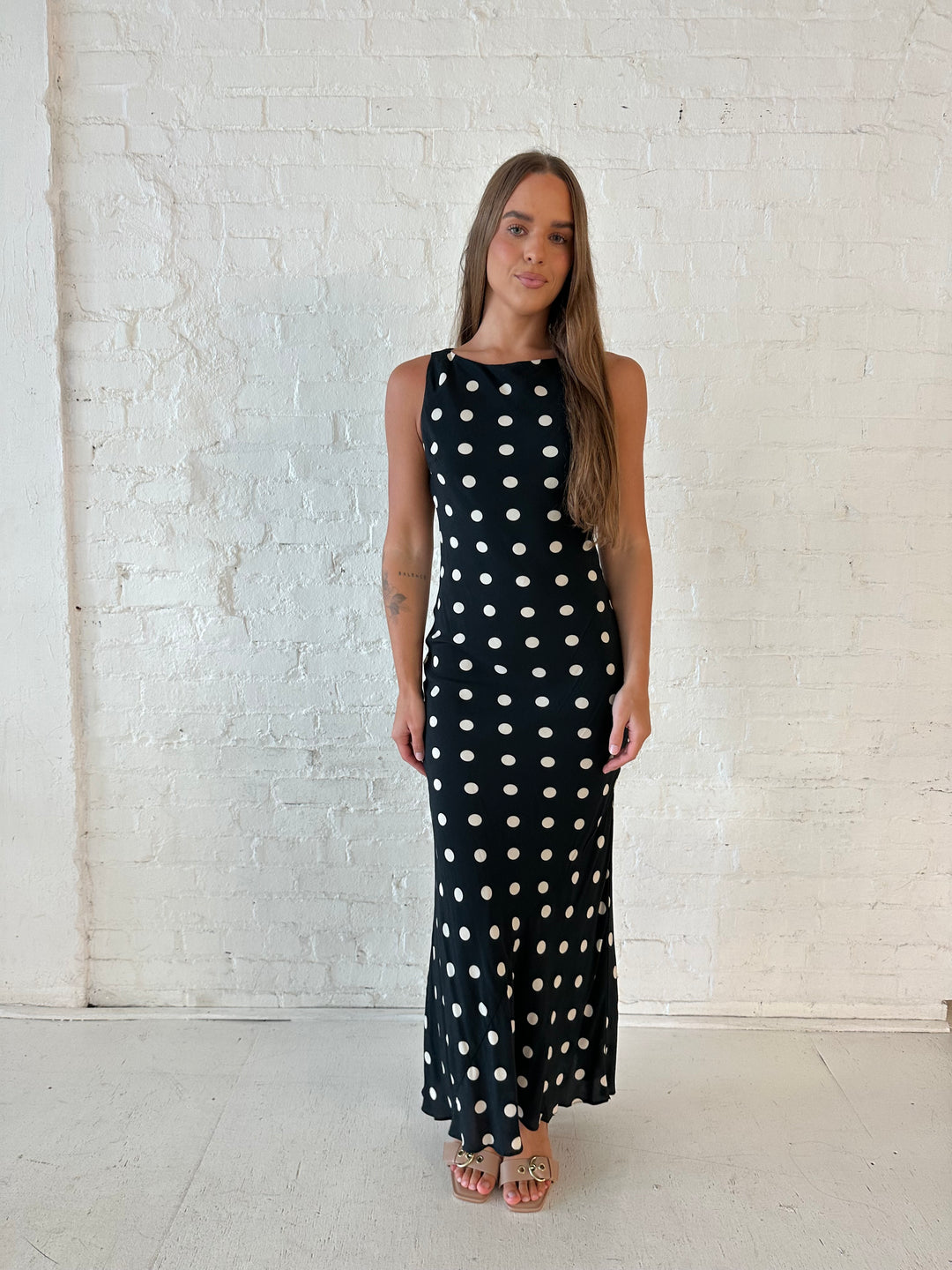 Woman wearing black and white polka dot high neck maxi dress with tan heels.