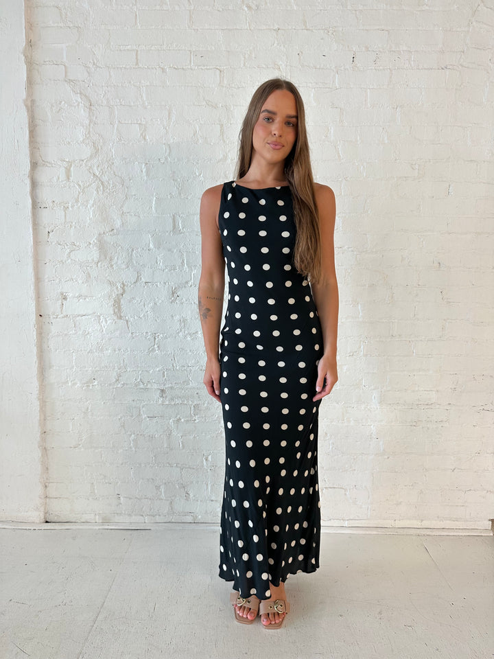 Woman wearing black and white polka dot high neck maxi dress with tan heels.