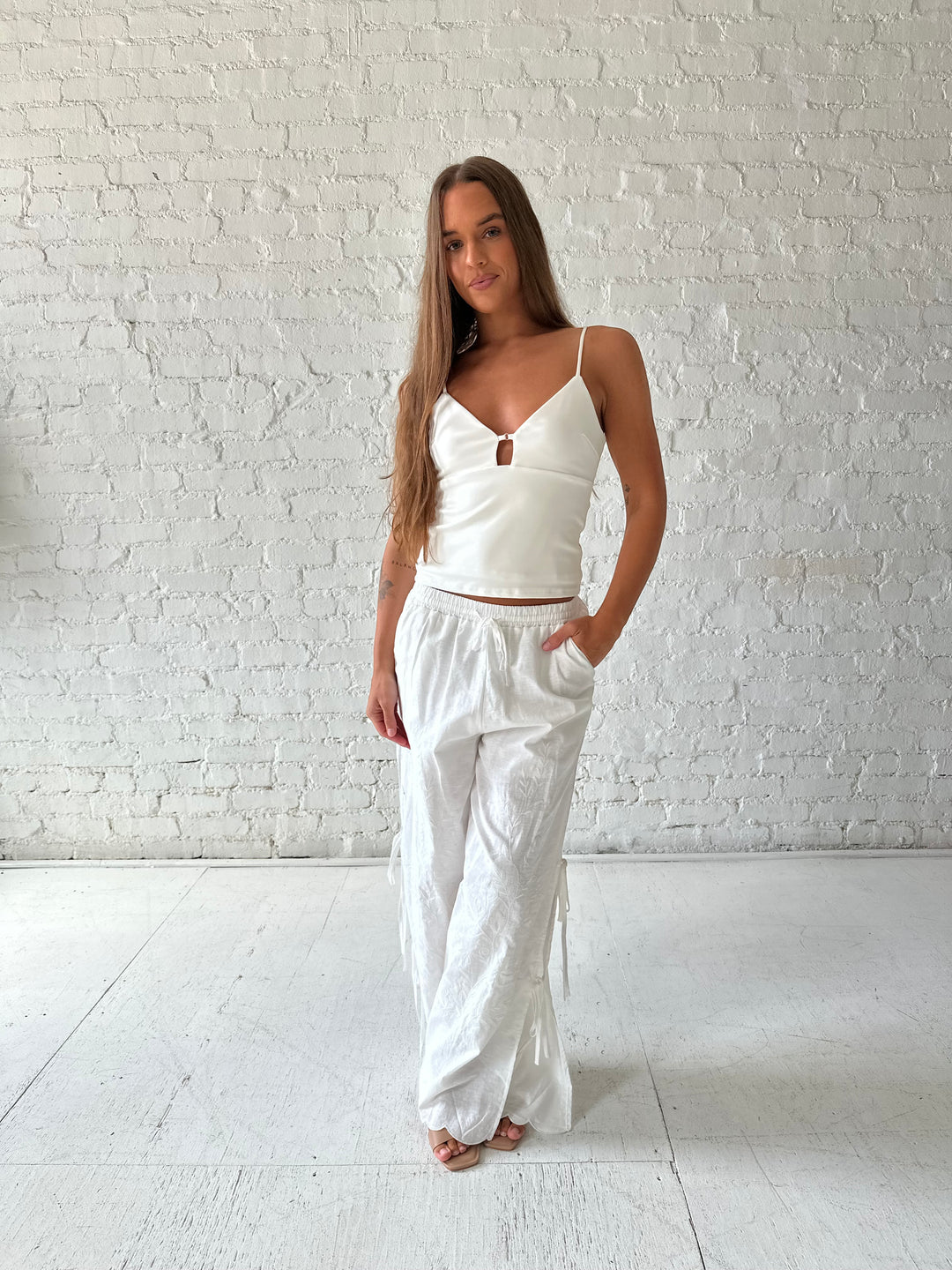 Woman wearing white embroidered wide leg pant with tie detail on the side. 