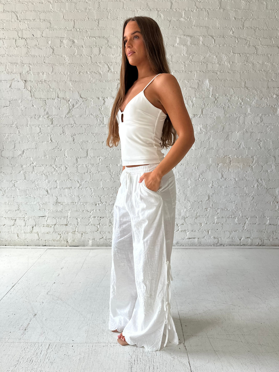 Woman wearing white embroidered wide leg pant with tie detail on the side. 