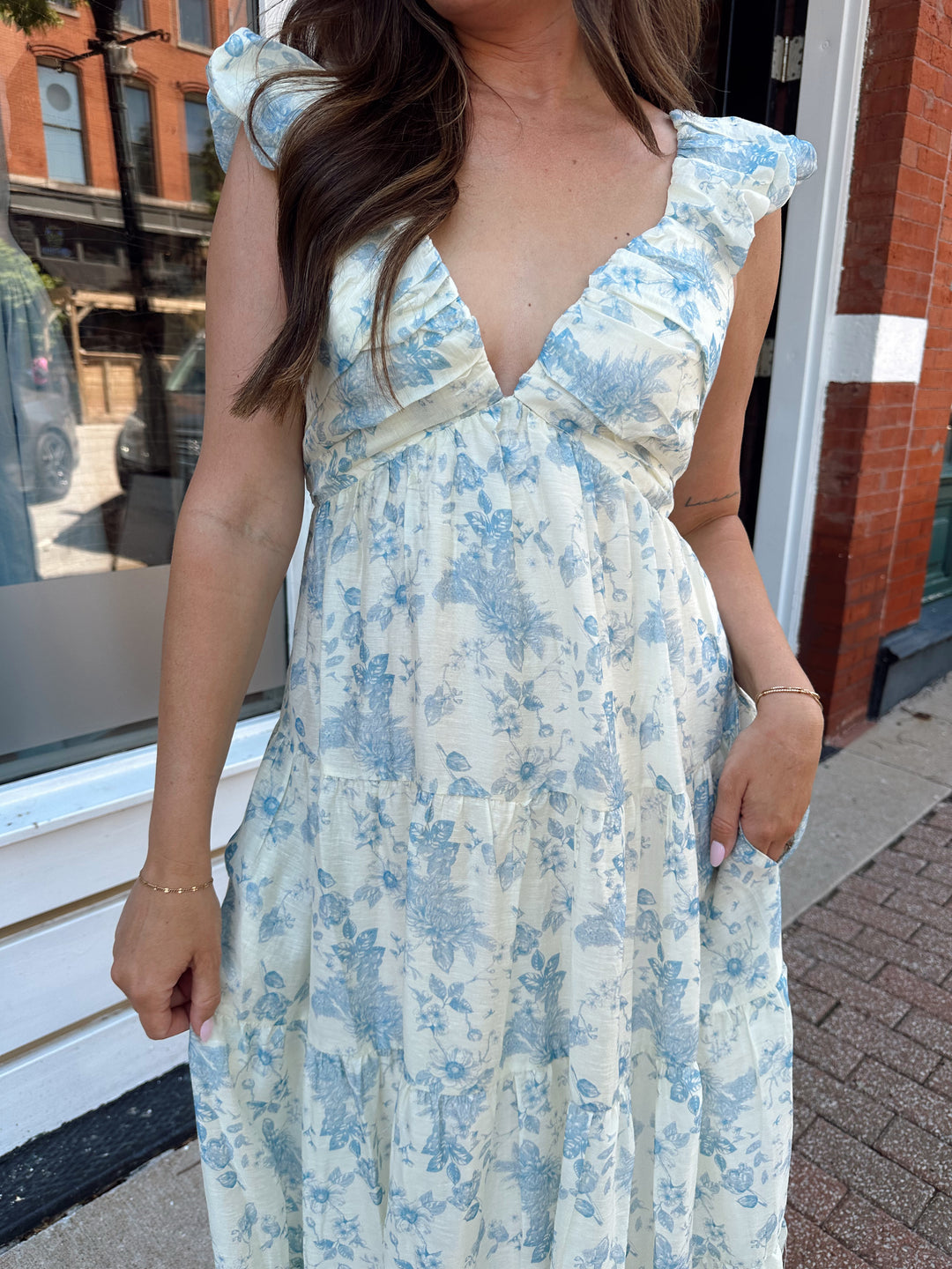 Woman wearing blue floral midi dress with pleated detail along neckline. 