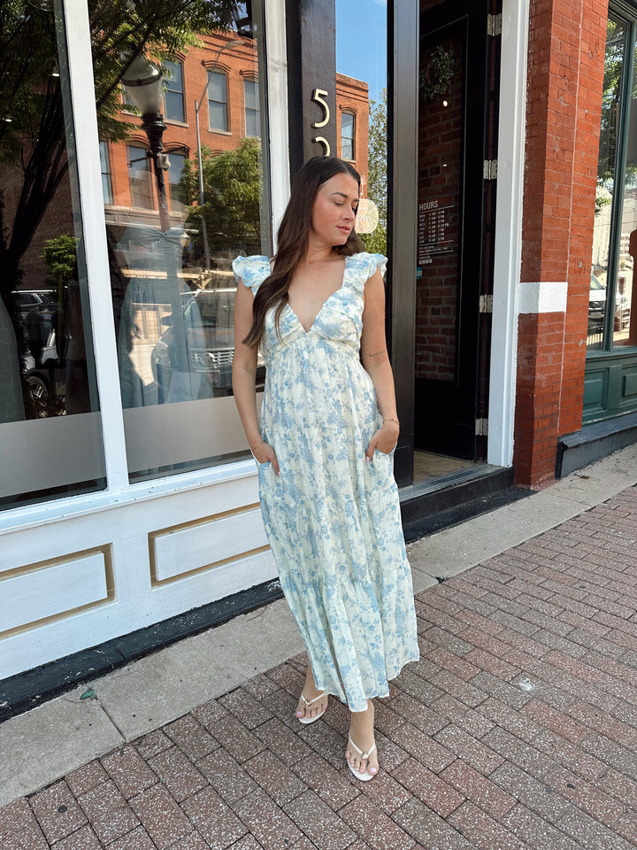Woman wearing blue floral midi dress with pleated detail along neckline. 