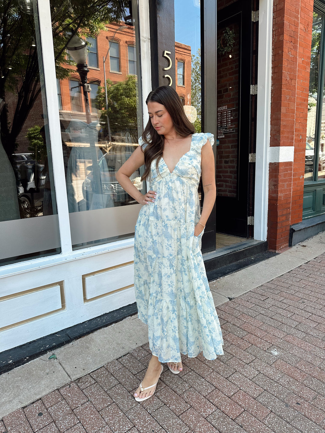 Woman wearing blue floral midi dress with pleated detail along neckline. 