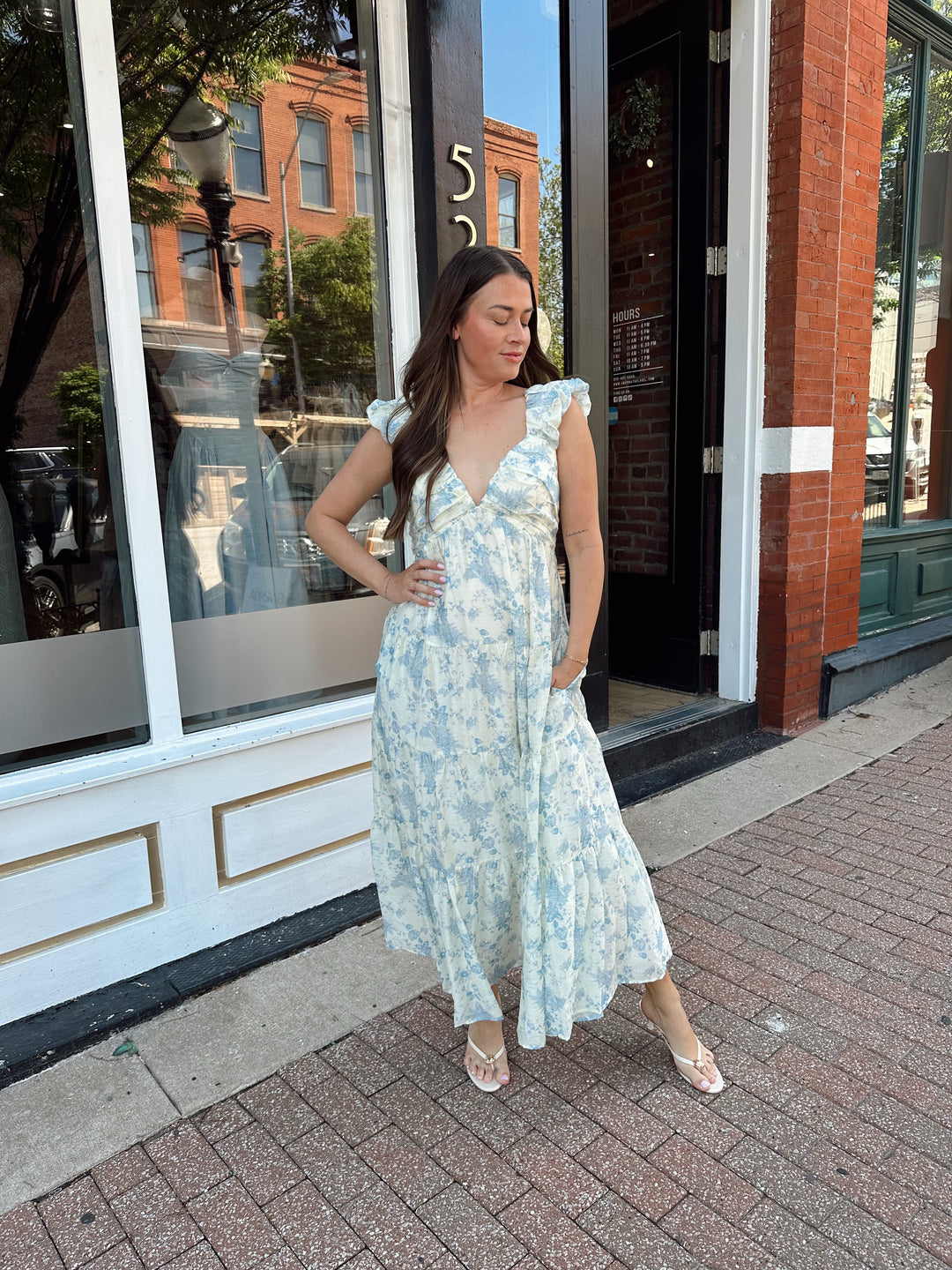 Woman wearing blue floral midi dress with pleated detail along neckline. 