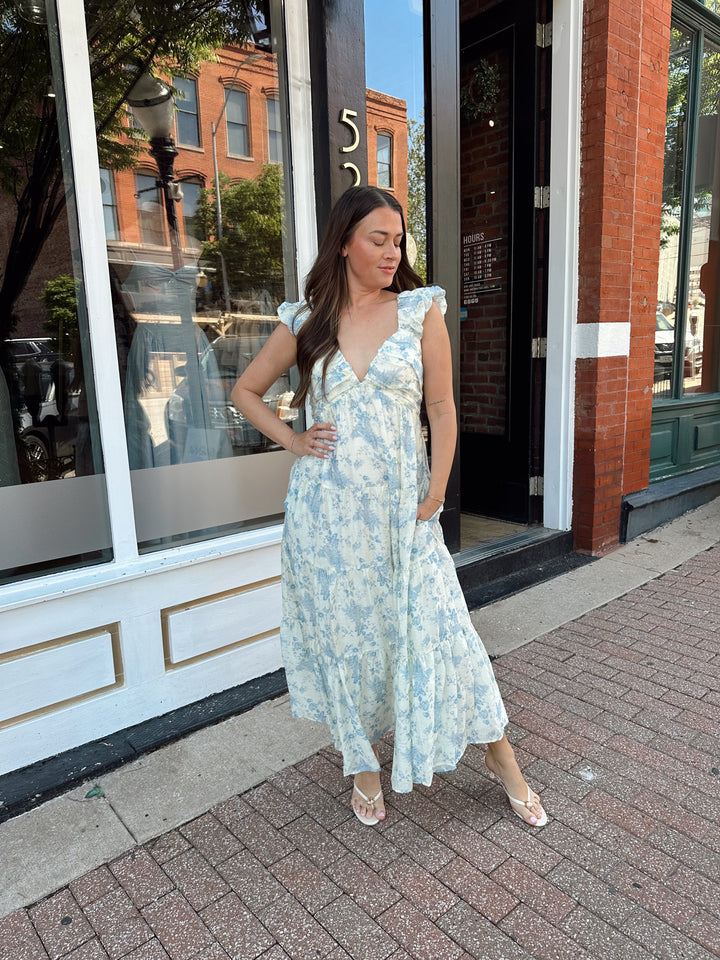 Woman wearing blue floral midi dress with pleated detail along neckline. 
