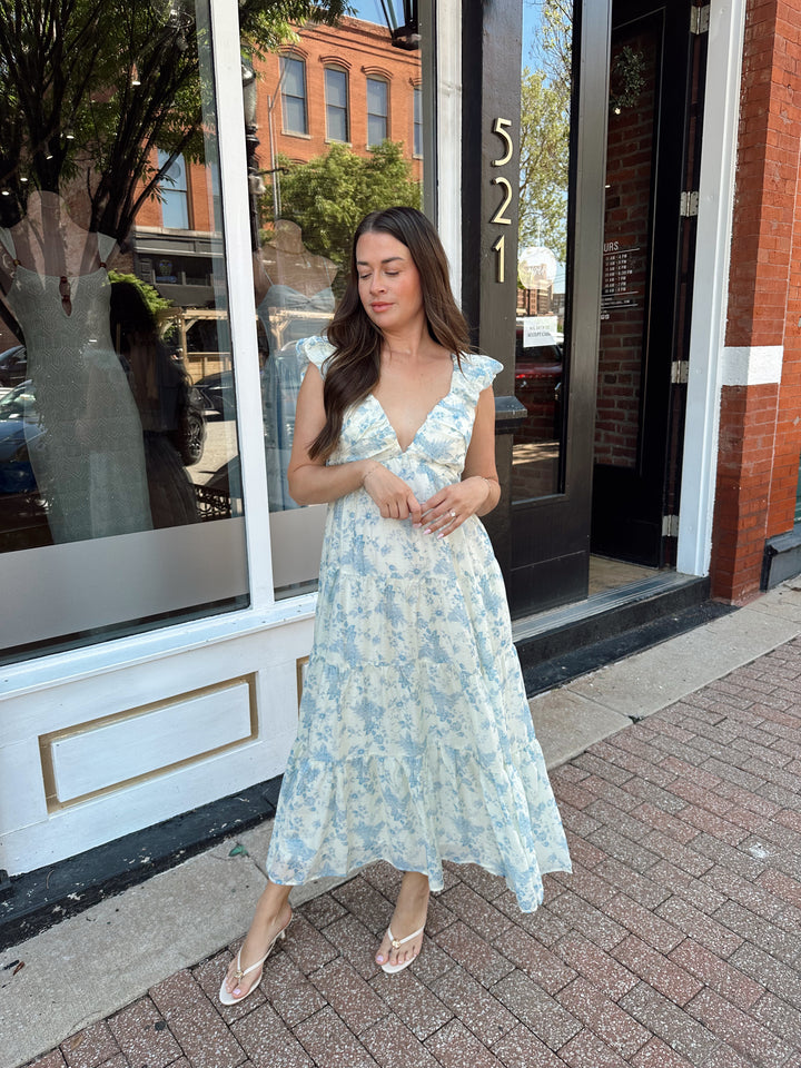 Woman wearing blue floral midi dress with pleated detail along neckline. 