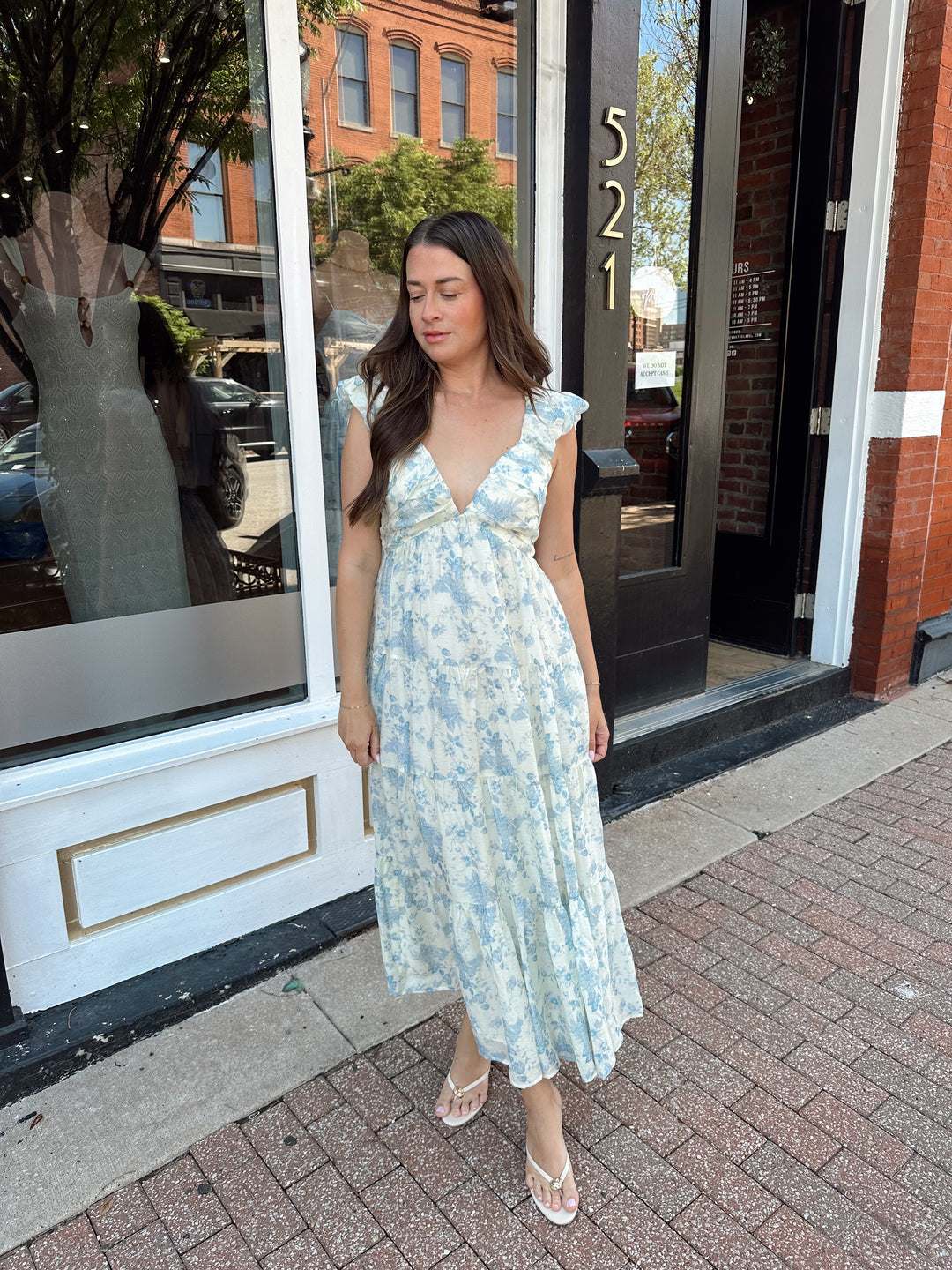 Woman wearing blue floral midi dress with pleated detail along neckline. 