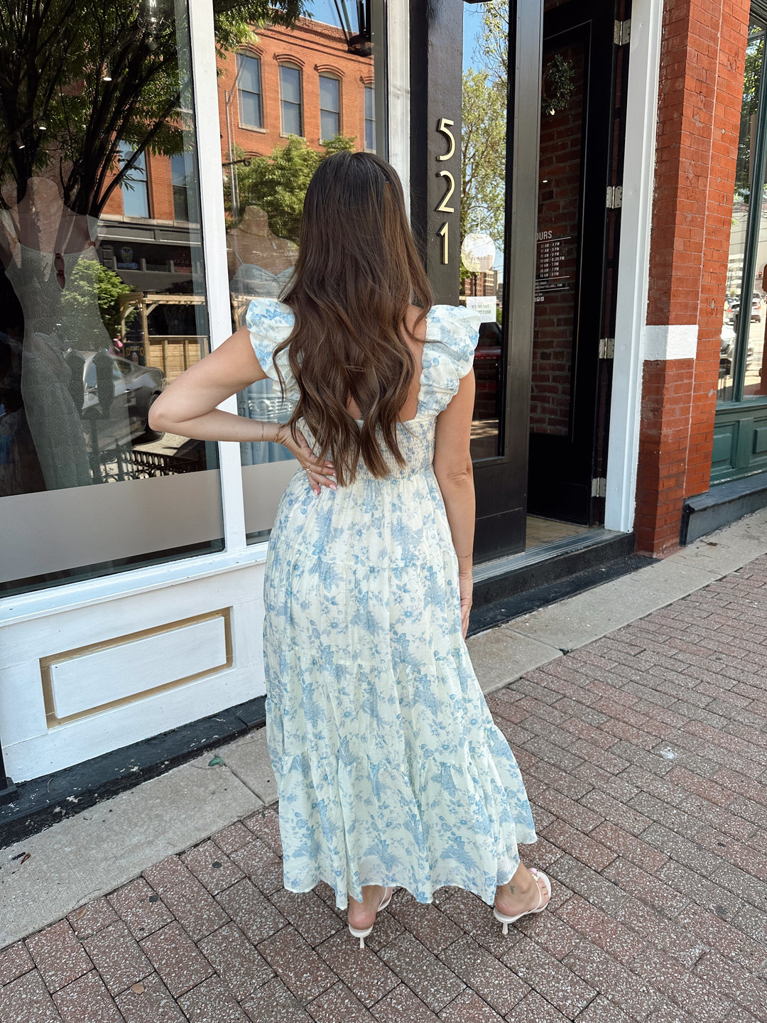 Woman wearing blue floral midi dress with pleated detail along neckline. 