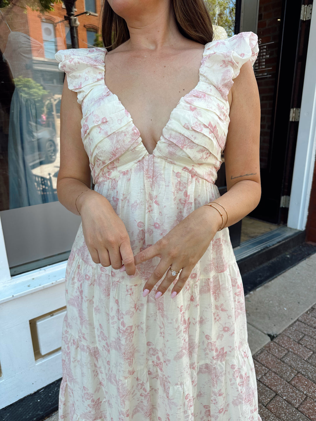 Woman wearing pink floral midi dress with ruched detail along the neckline. 