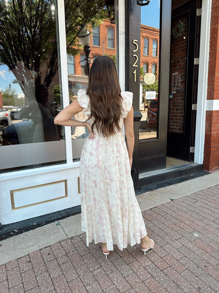 Woman wearing pink floral midi dress with ruched detail along the neckline. 