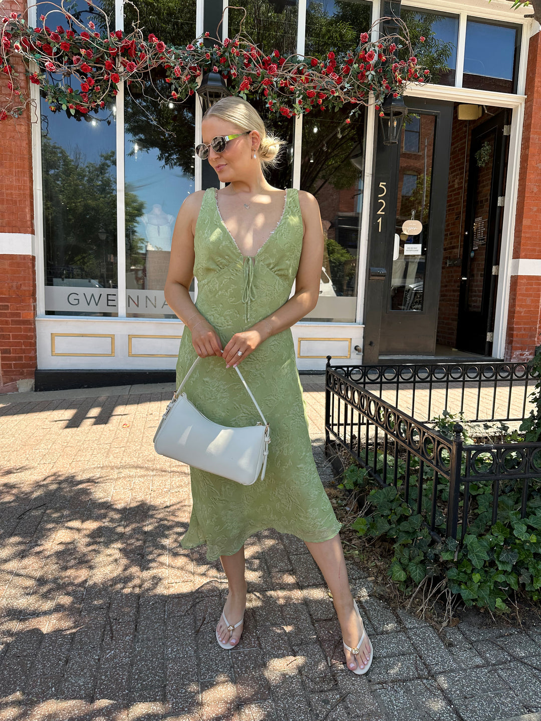 Woman wearing light green floral midi dress with v-neckline, and beaded trim detailing. 