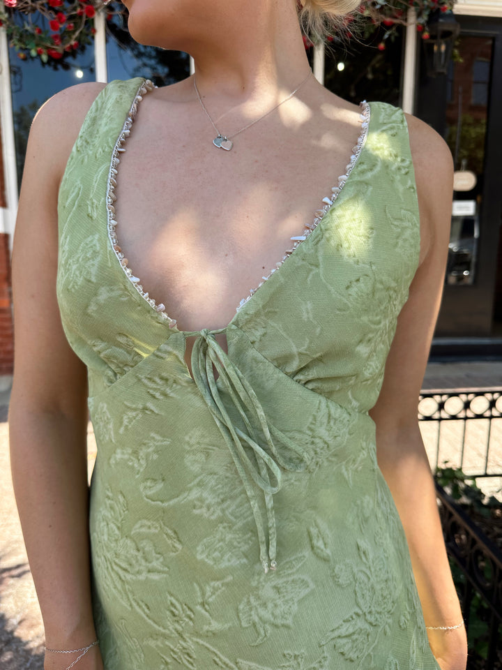 Woman wearing light green floral midi dress with v-neckline, and beaded trim detailing. 