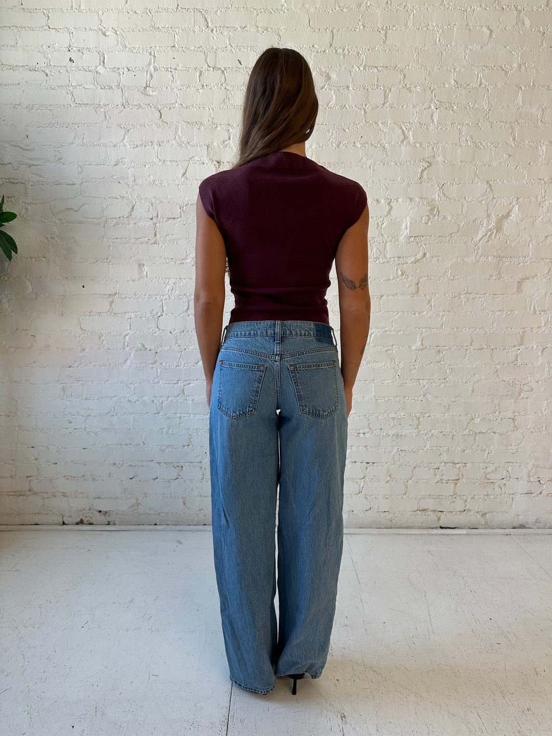 Woman wearing plum colored ribbed cap sleeve top with high neckline, and medium wash jean. 