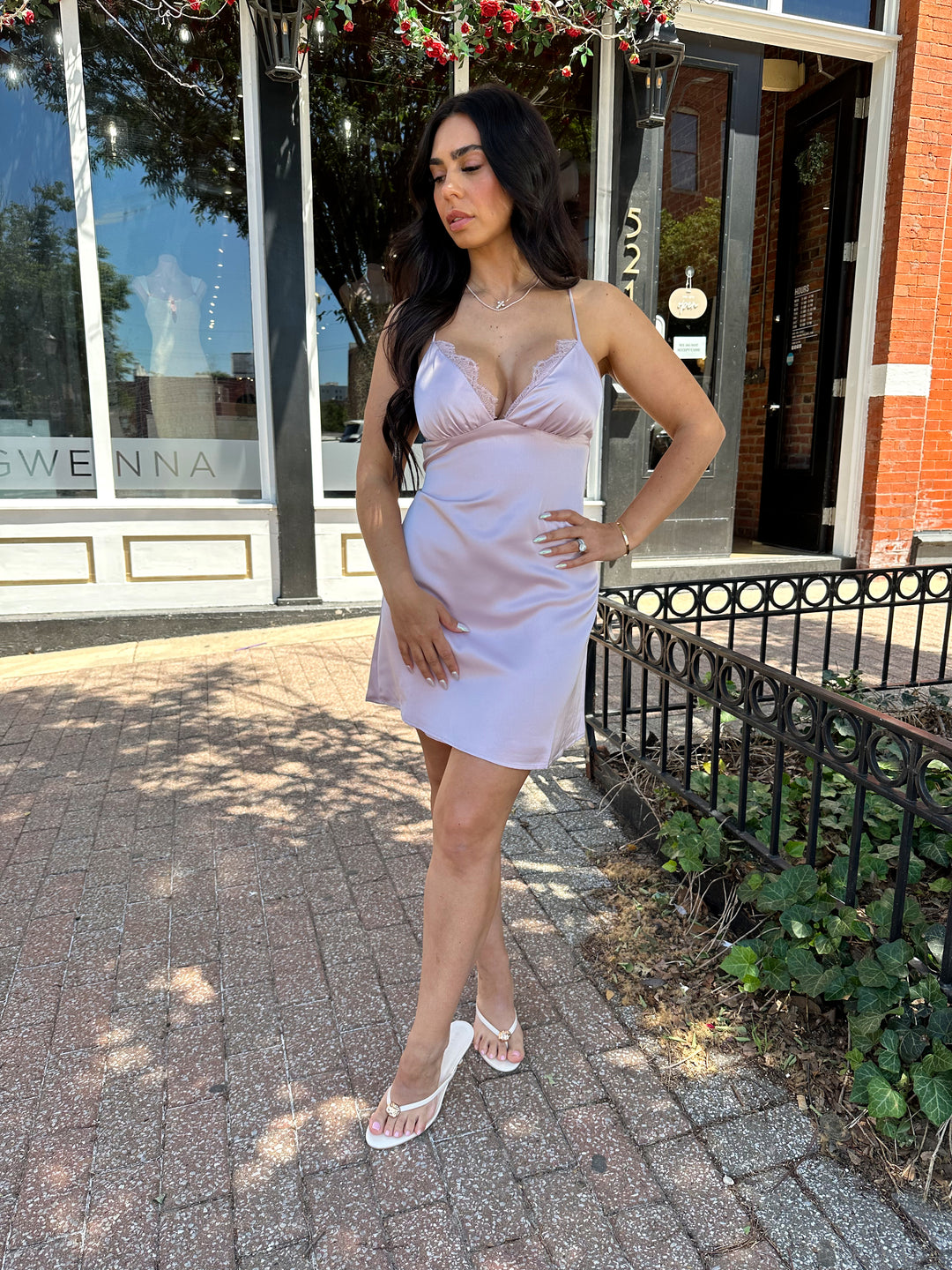 Woman wearing lavender satin mini dress with lace trim detailing, open back, and self tie criss-cross straps.