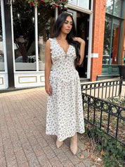 Woman wearing oatmeal midi dress with floral pattern and ruffle detail.