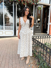 Woman wearing oatmeal midi dress with floral pattern and ruffle detail.