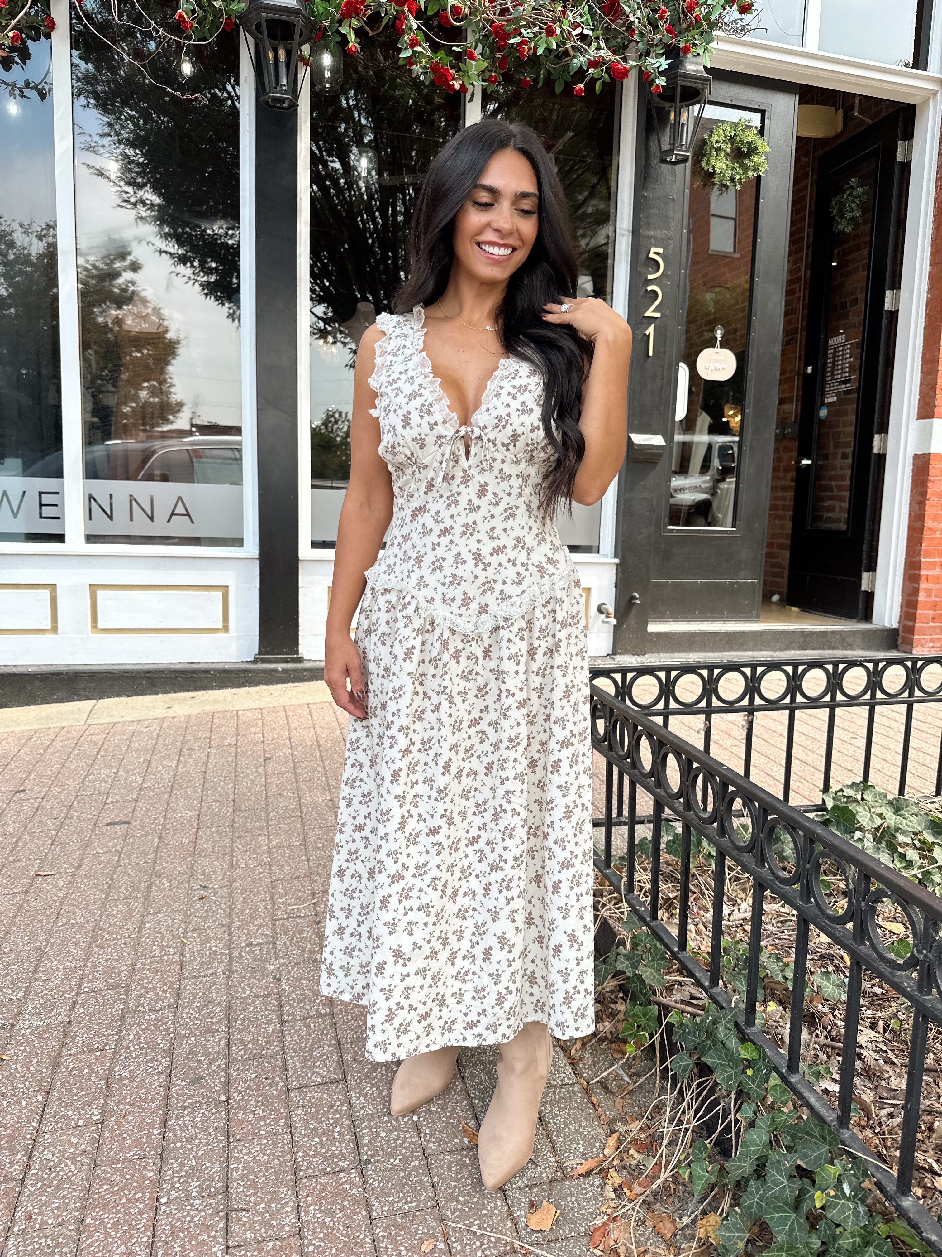 Woman wearing oatmeal midi dress with floral pattern and ruffle detail.