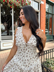 Woman wearing oatmeal midi dress with floral pattern and ruffle detail.