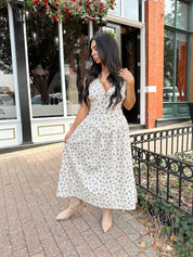 Woman wearing oatmeal midi dress with floral pattern and ruffle detail.